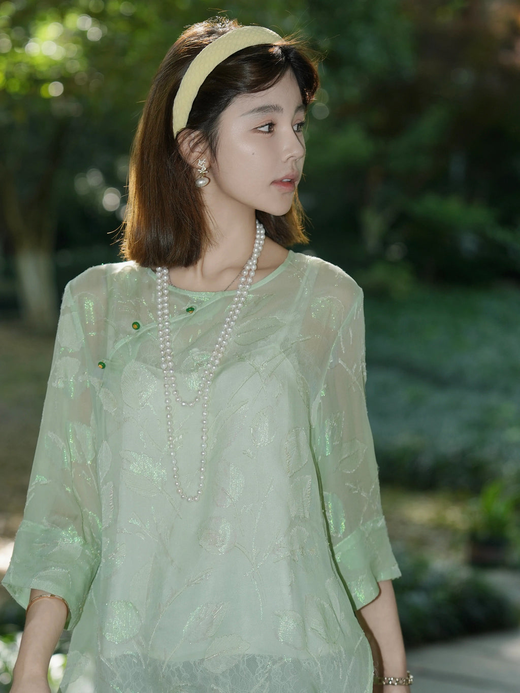 Side profile of a model wearing a mint green silk top with a round neckline