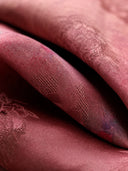 Close-up of lustrous mulberry-rose silk fabric with subtle woven texture and floral details.