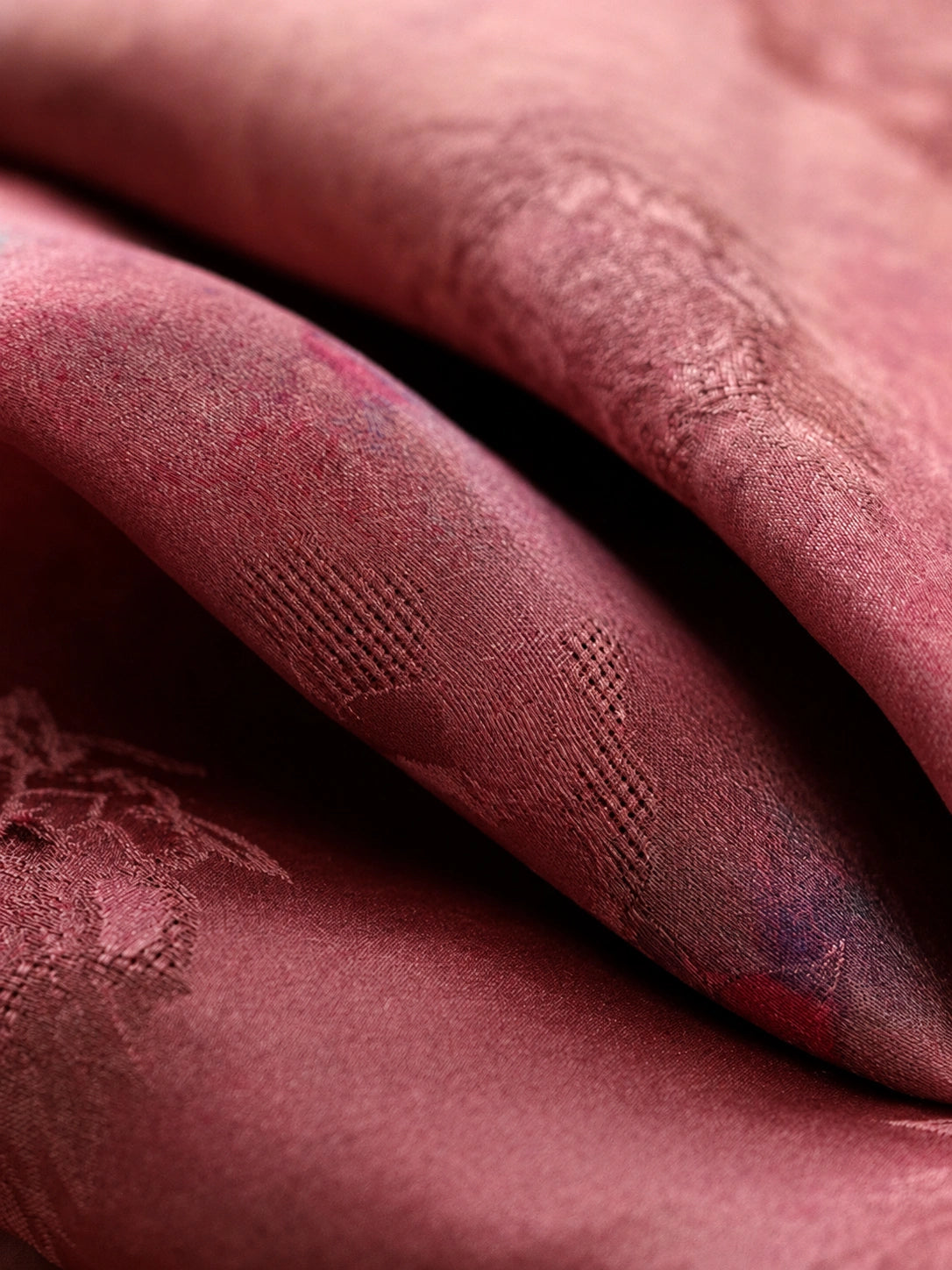 Close-up of lustrous mulberry-rose silk fabric with subtle woven texture and floral details.