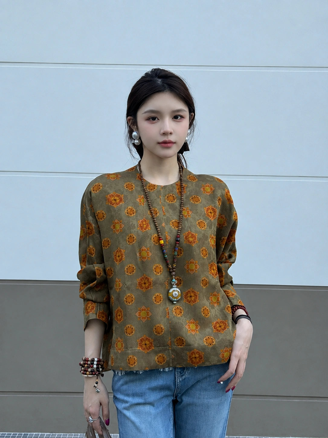 Model styling an olive floral silk top with blue jeans and accessories