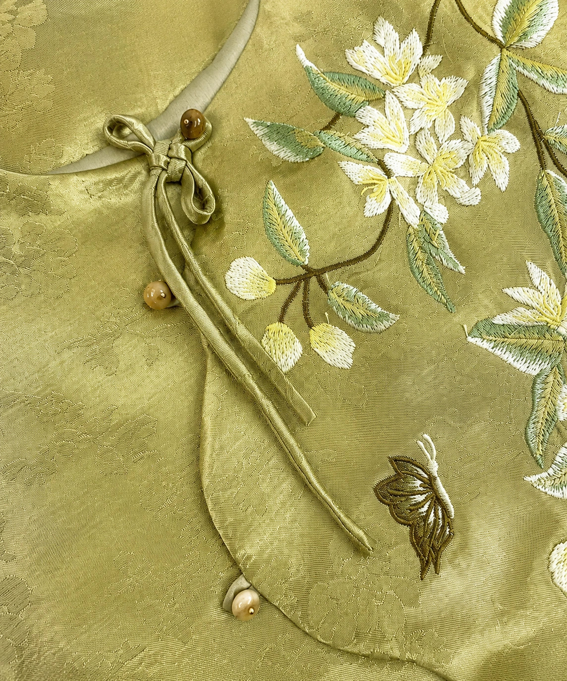 Close-up of floral and butterfly embroidery with knotted tie and bead-style closures