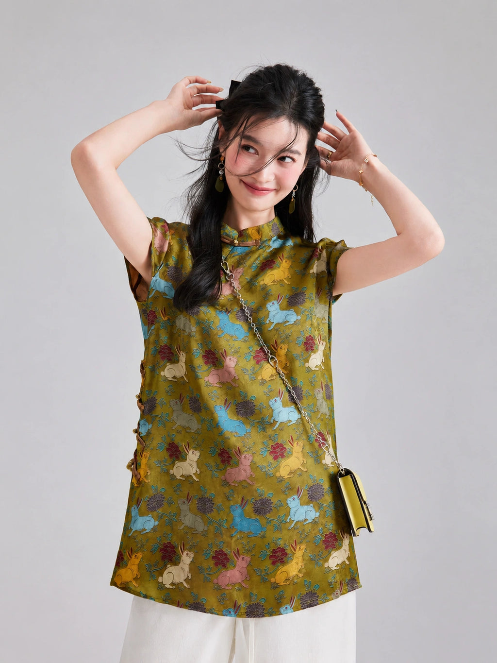 Model wearing an olive-gold Gambiered Silk top with blue, pink, yellow and ivory rabbits among flowers