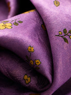 Close-up of lustrous orchid-purple silk with tonal texture and golden floral motifs.