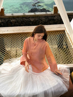 Model wearing a peach pink Chinese-inspired silk top with long sleeves and a relaxed silhouette