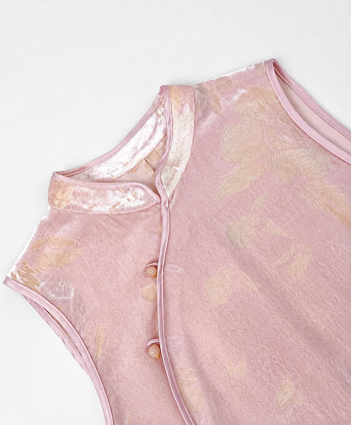 Blush-pink cut-velvet vest showing its Mandarin collar, asymmetric piping and decorative frog-button closures