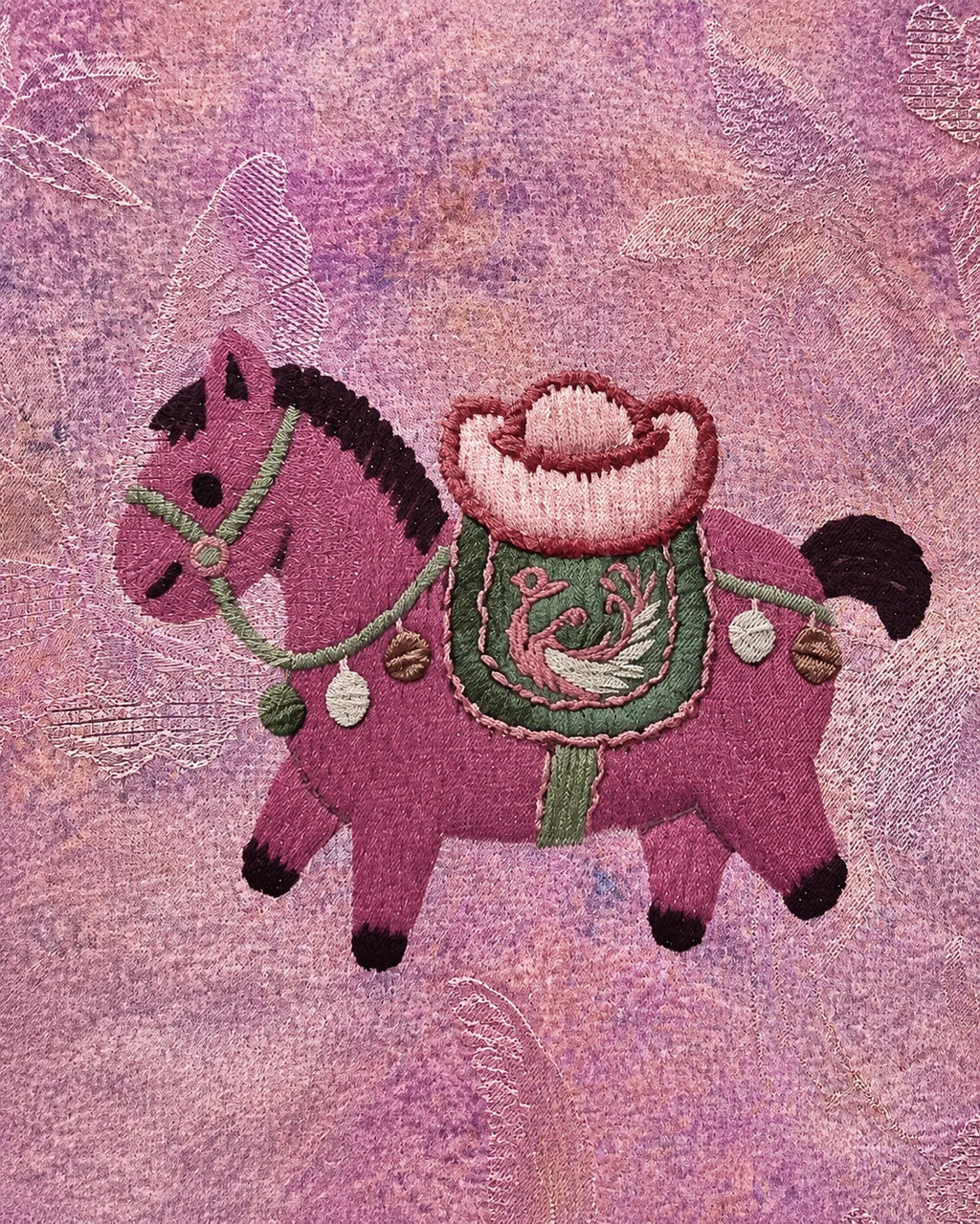 Detailed close-up of a pink embroidered horse motif on the textured dusty rose jacquard fabric