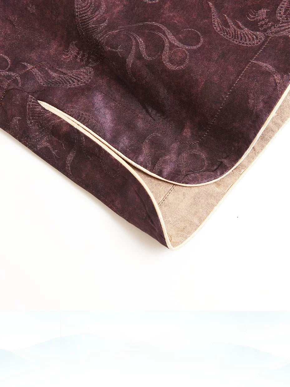 Detail of the curved hem, gold piping and paisley texture on a plum silk-blend top