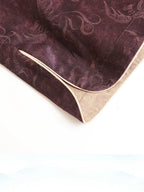 Detail of the curved hem, gold piping and paisley texture on a plum silk-blend top