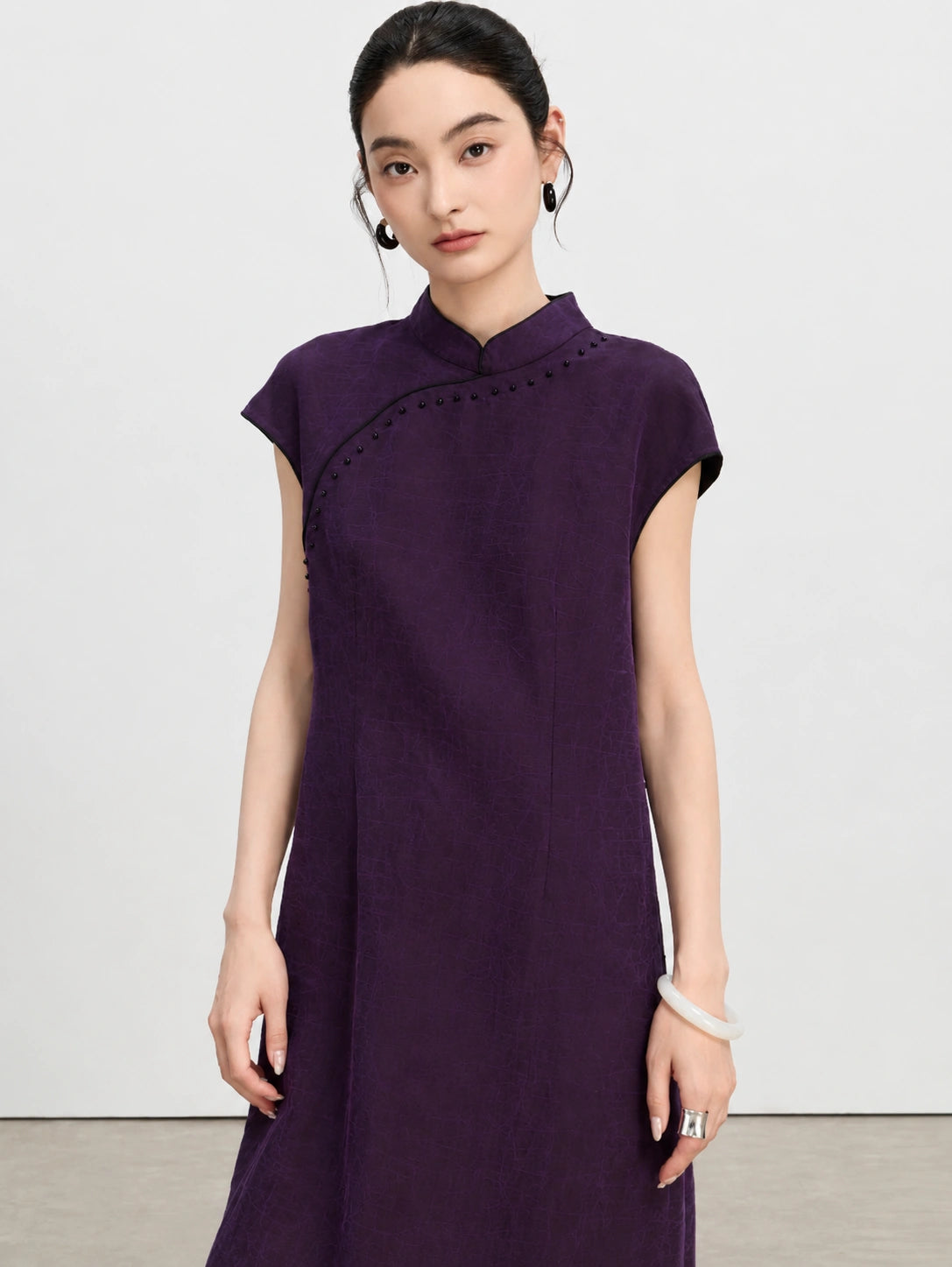 Close view of a woman wearing a purple crackle-textured silk qipao dress with black bead detailing.