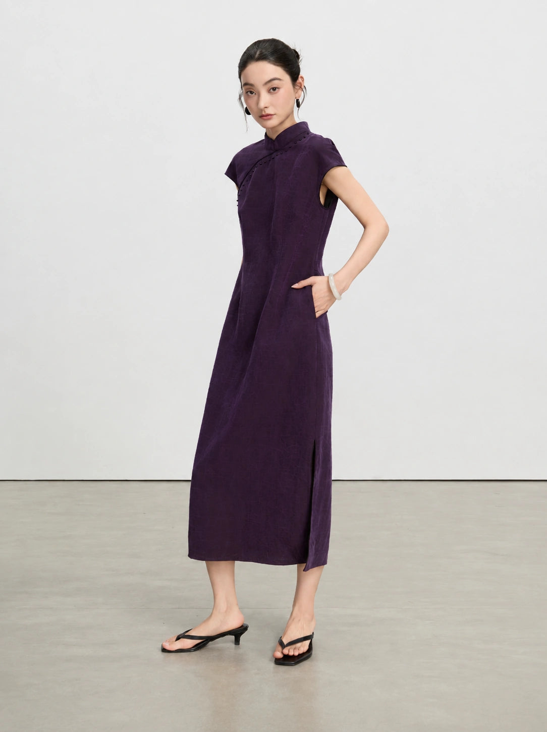 Full-length view of an aubergine New Chinese qipao dress with side pockets and a side slit.