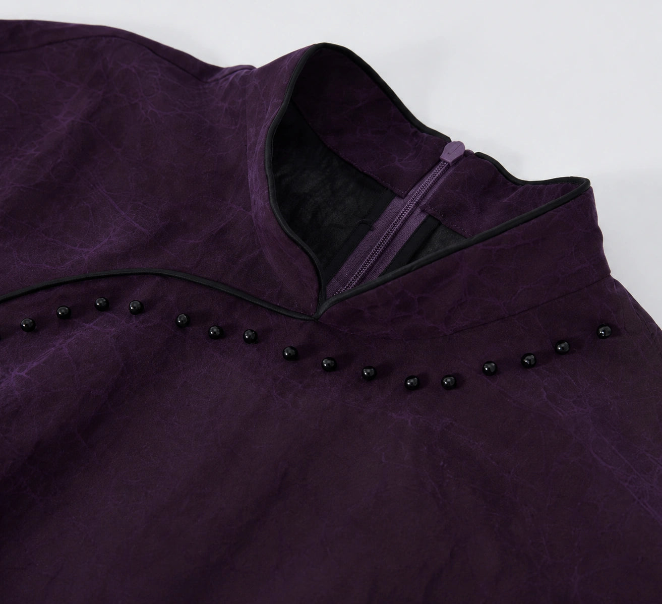Close-up of the Mandarin collar, black piping and bead embellishment on a purple silk qipao dress.