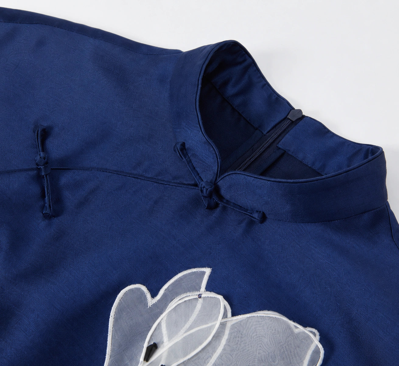 Close-up of the navy qipao stand collar, knotted frog closures and magnolia embroidery