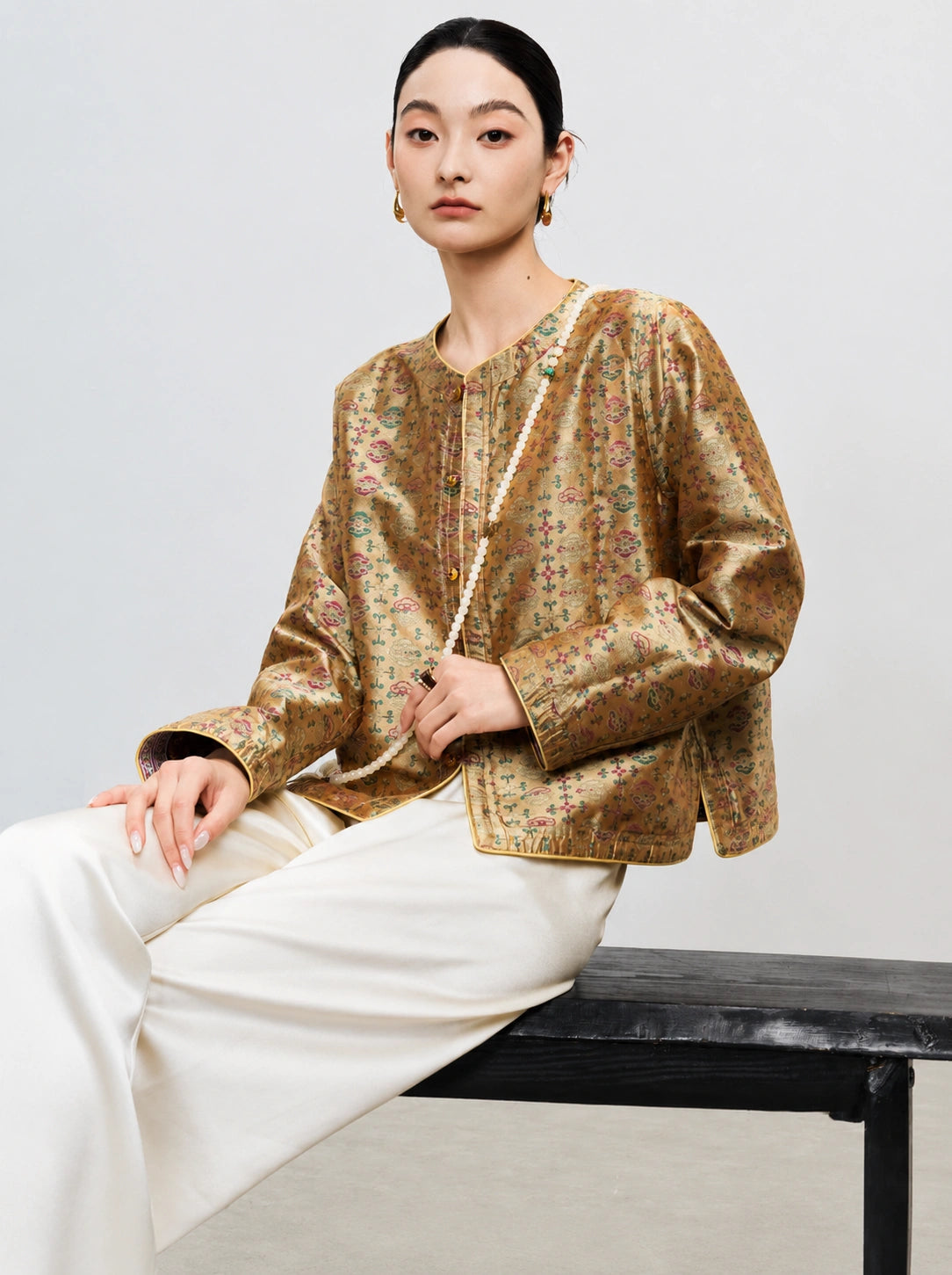 Close-up of the antique gold silk jacket showing its lustrous Shu brocade motifs and button front.