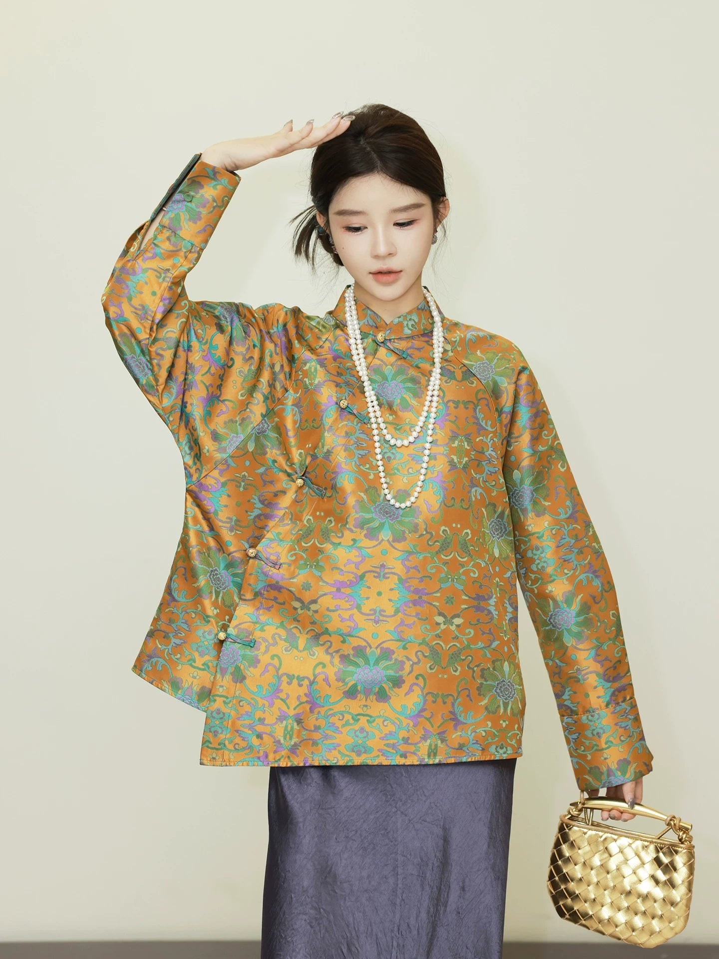 Model styling a loose reversible silk jacket with a vibrant ornamental pattern and pearl necklace
