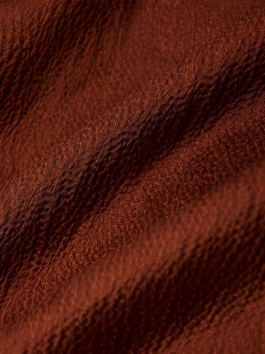 Close-up of the lustrous textured surface of rust-brown 100% mulberry silk fabric.