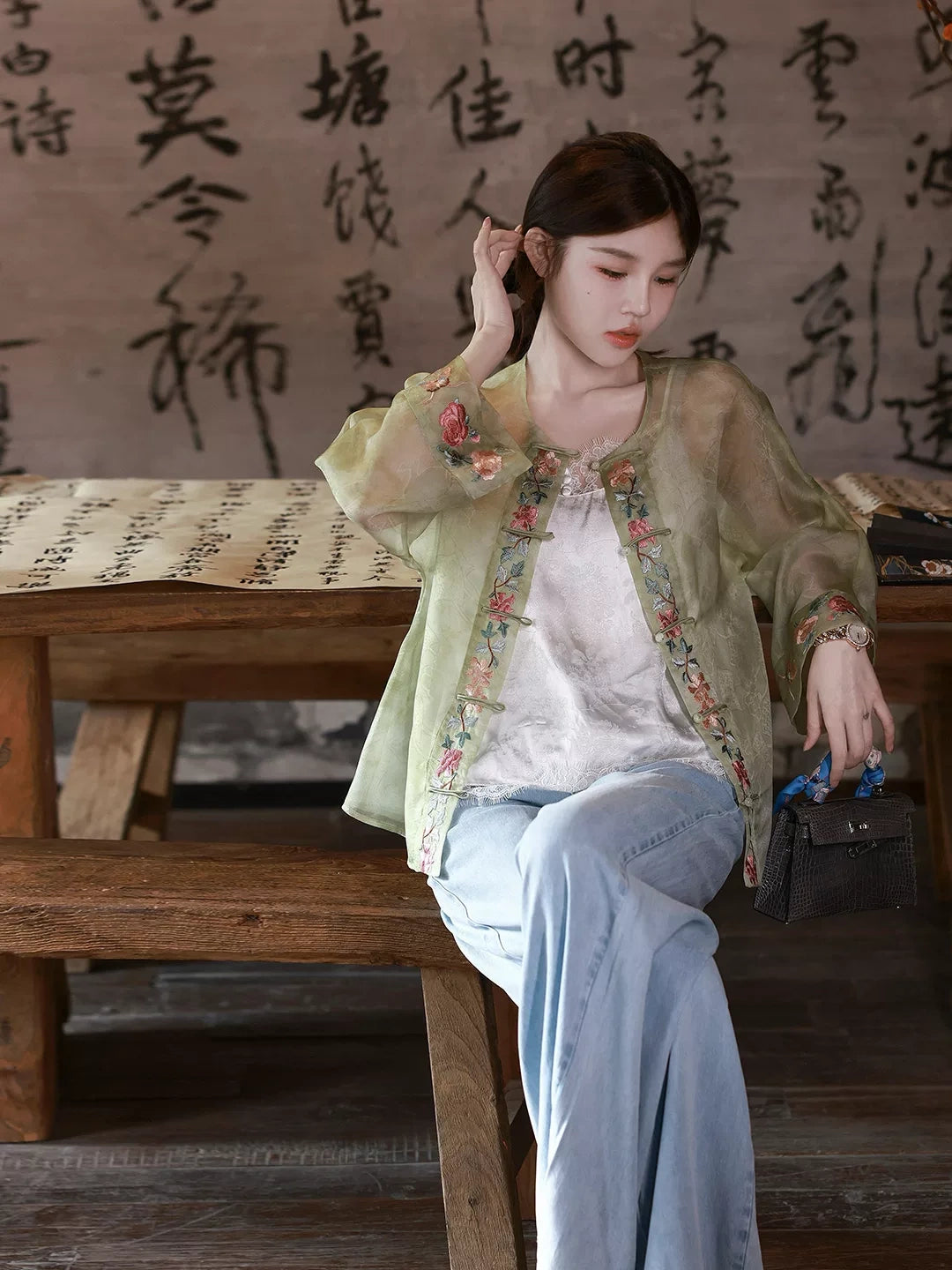 Model wearing a sage green embroidered mulberry silk overshirt over a white top and light blue jeans