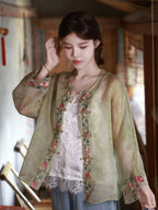 Close-up of a sage green silk overshirt showing floral embroidery and the front placket