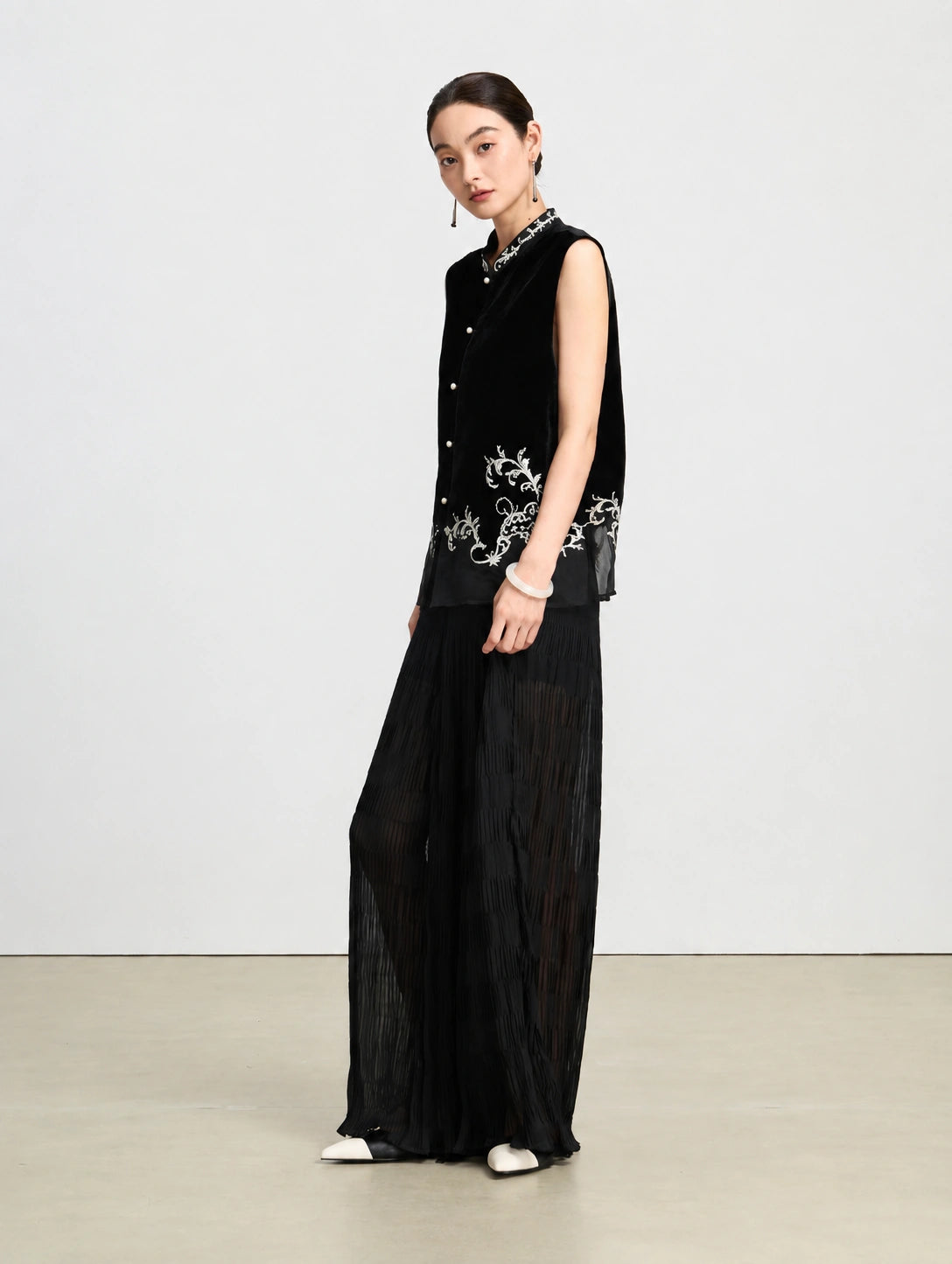 Side view of a black embroidered velvet vest showing its relaxed silhouette and translucent silk hem.