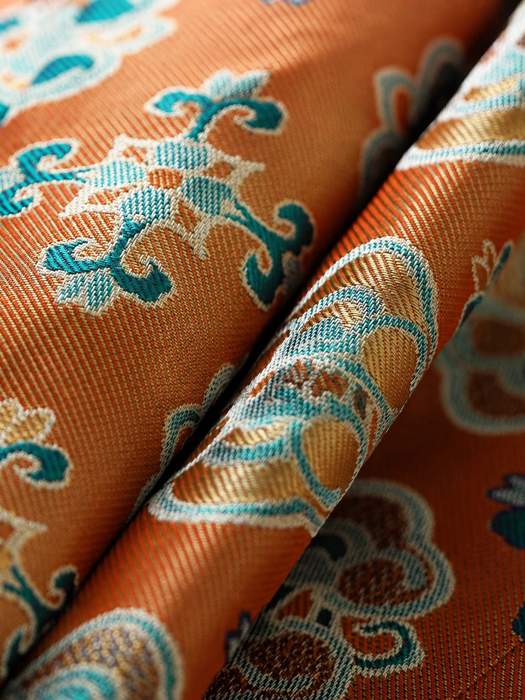 Close-up of orange-gold Shu brocade silk fabric with turquoise and ivory floral motifs