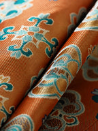 Close-up of orange-gold Shu brocade silk fabric with turquoise and ivory floral motifs