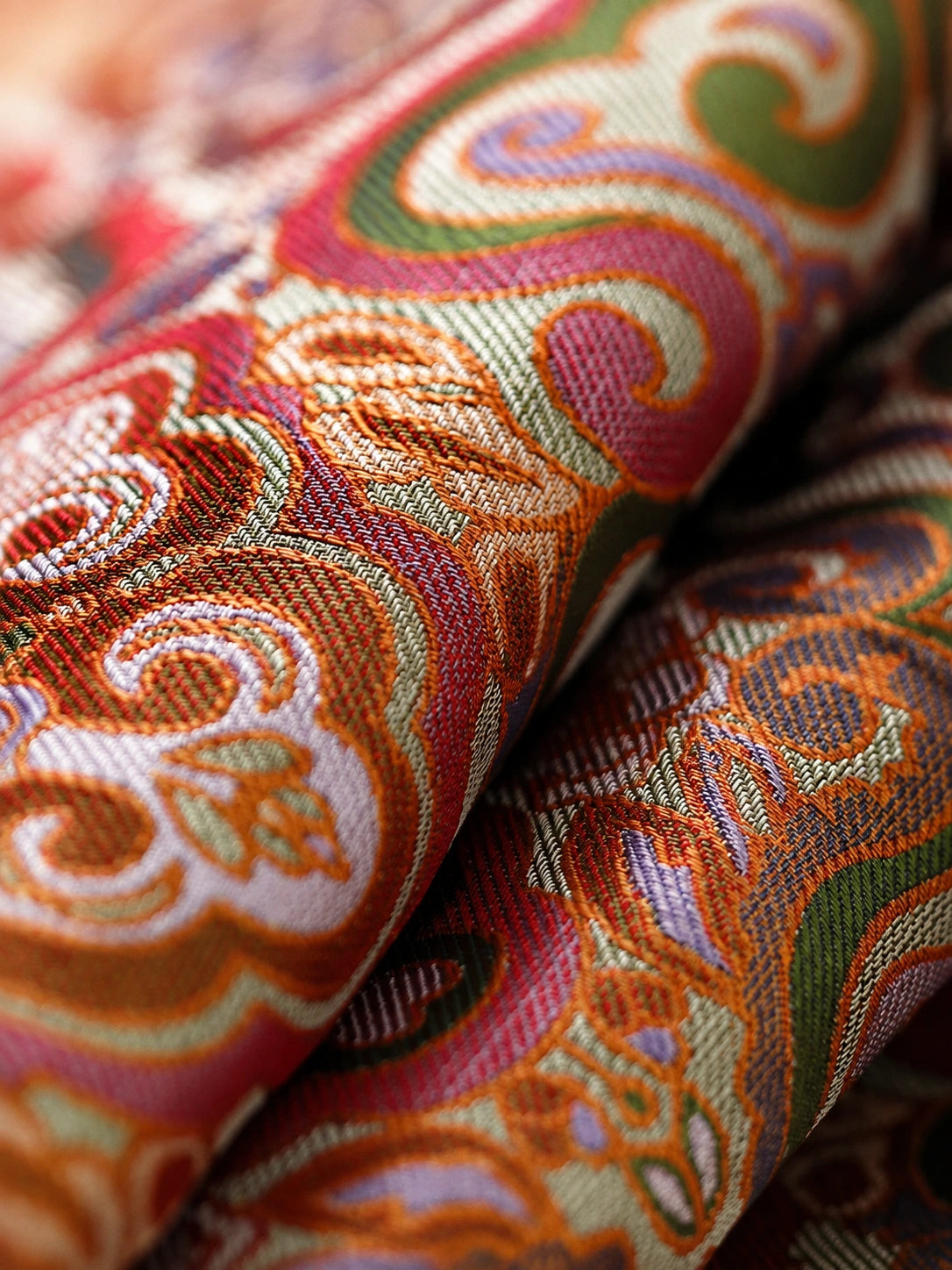 Close-up of multicolored Shu brocade silk woven with terracotta, olive, orange, lavender and cream motifs.