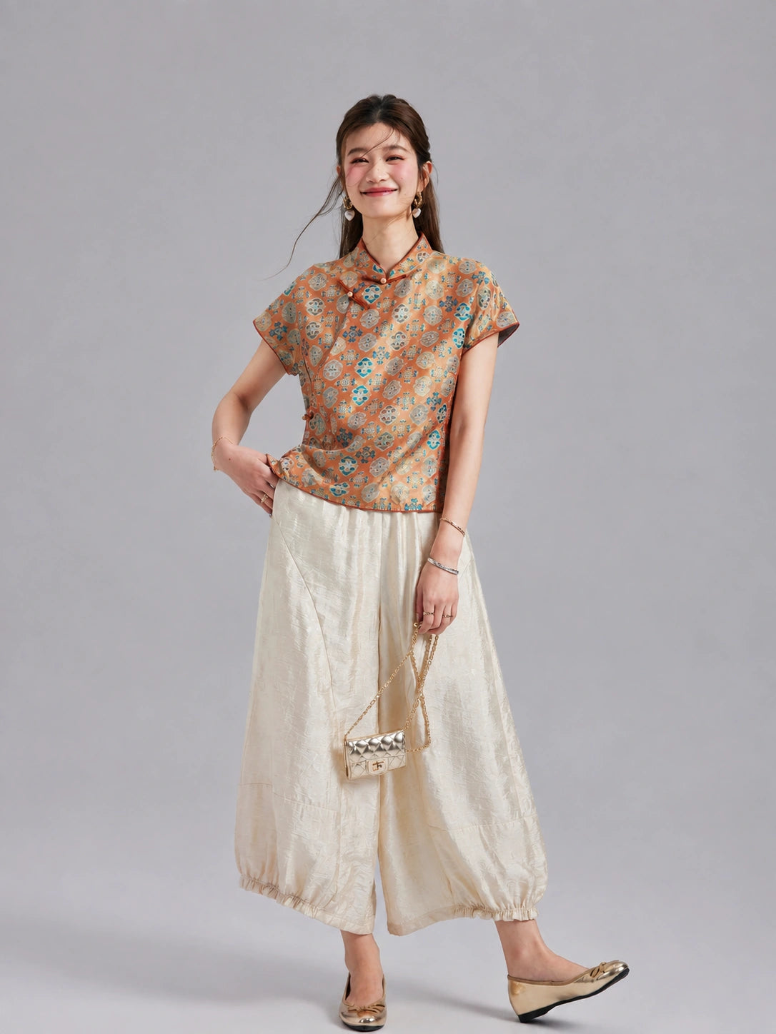 Model wearing a Gambiered Silk orange-gold Shu brocade top with ivory wide-leg trousers