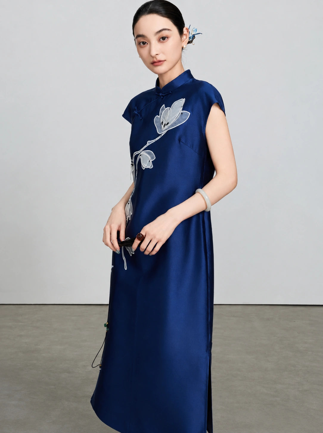 Three-quarter view showing the smooth silk-wool fabric and magnolia embroidery of the navy qipao
