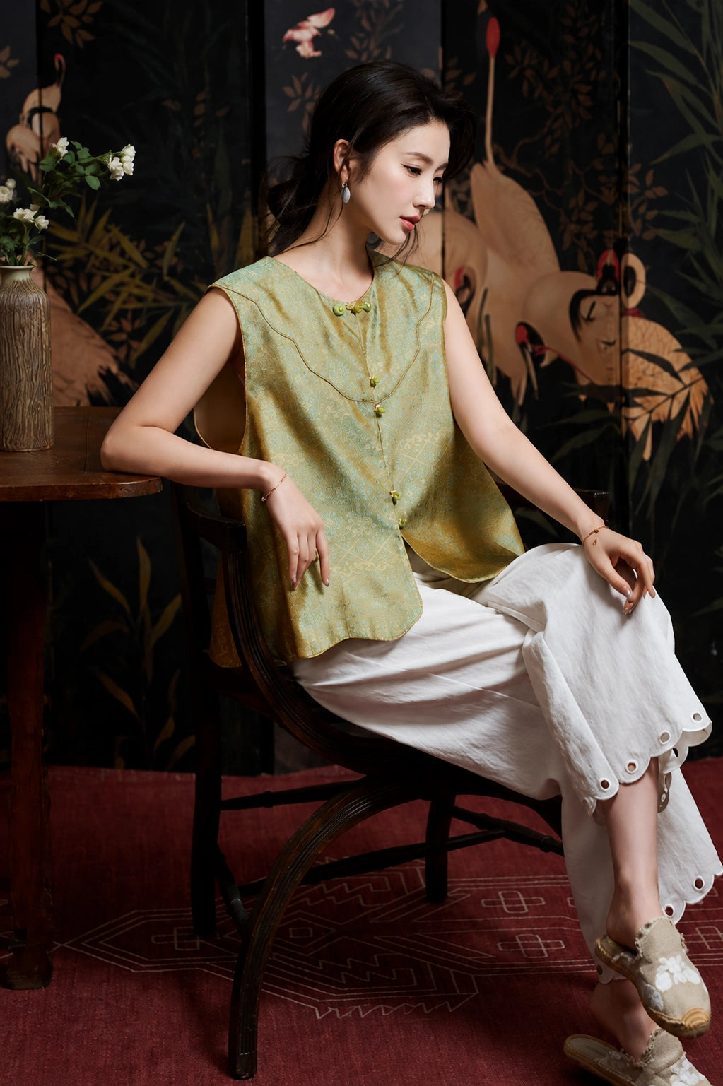 Seated model styling the celadon sleeveless silk vest with white wide-leg trousers