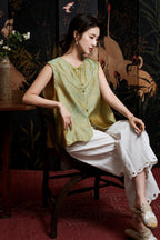 Seated model styling the celadon sleeveless silk vest with white wide-leg trousers