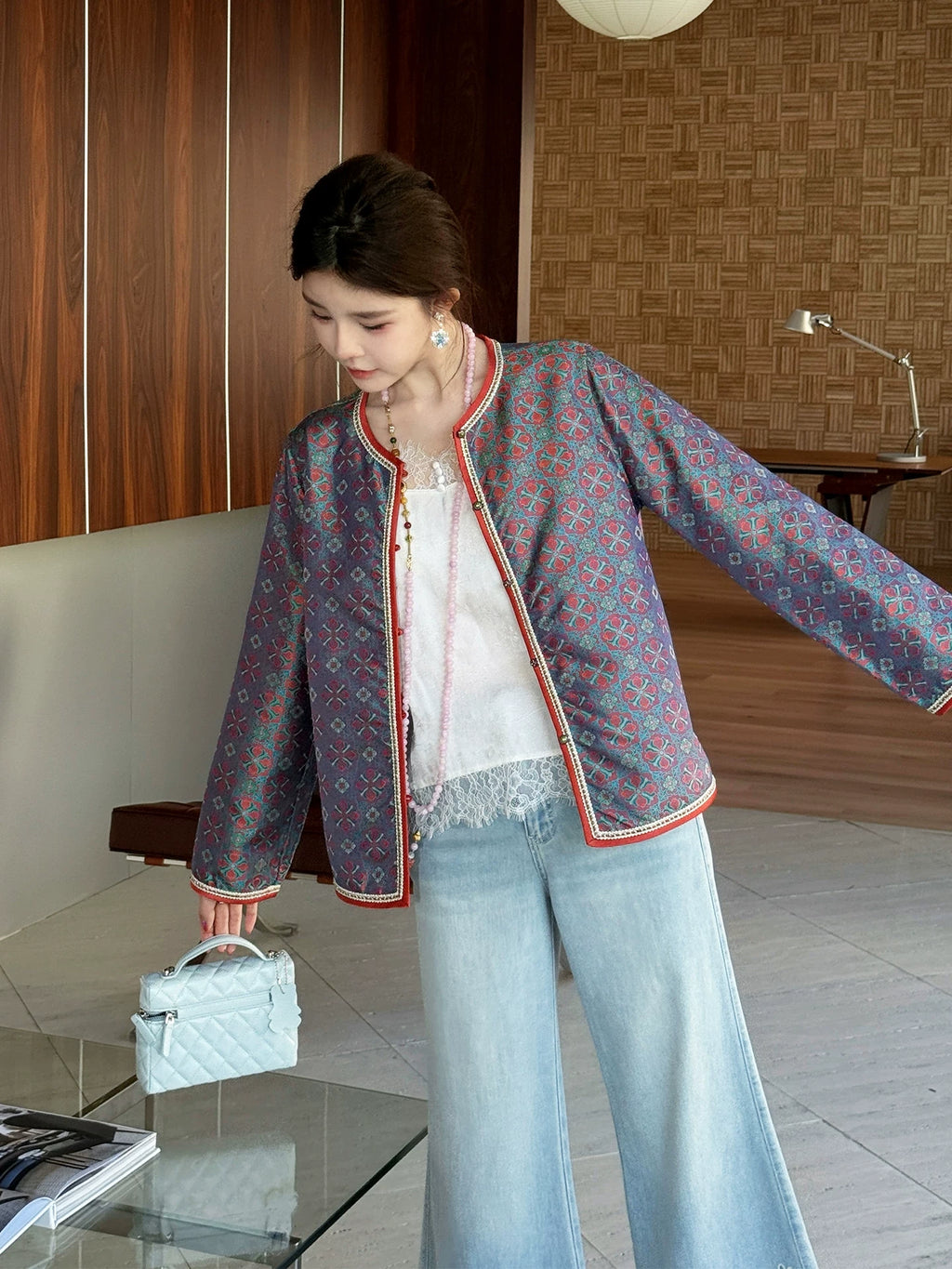 Model wearing a fitted teal Chinese-inspired silk jacket with red trim and straight sleeves
