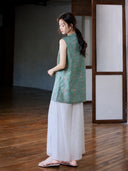 Back three-quarter view of the teal and pink Song brocade longline vest styled with white trousers