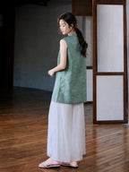 Back three-quarter view of the teal and pink Song brocade longline vest styled with white trousers