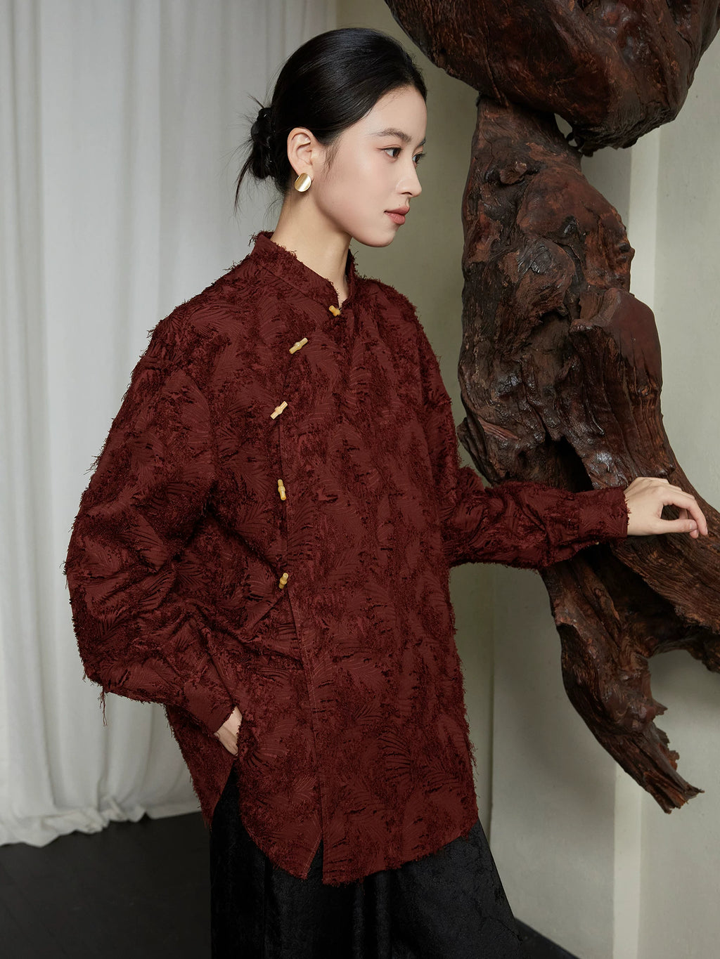 Three-quarter side view of the burgundy textured Mandarin collar blouse featuring a relaxed silhouette and asymmetrical frog-button closure.
