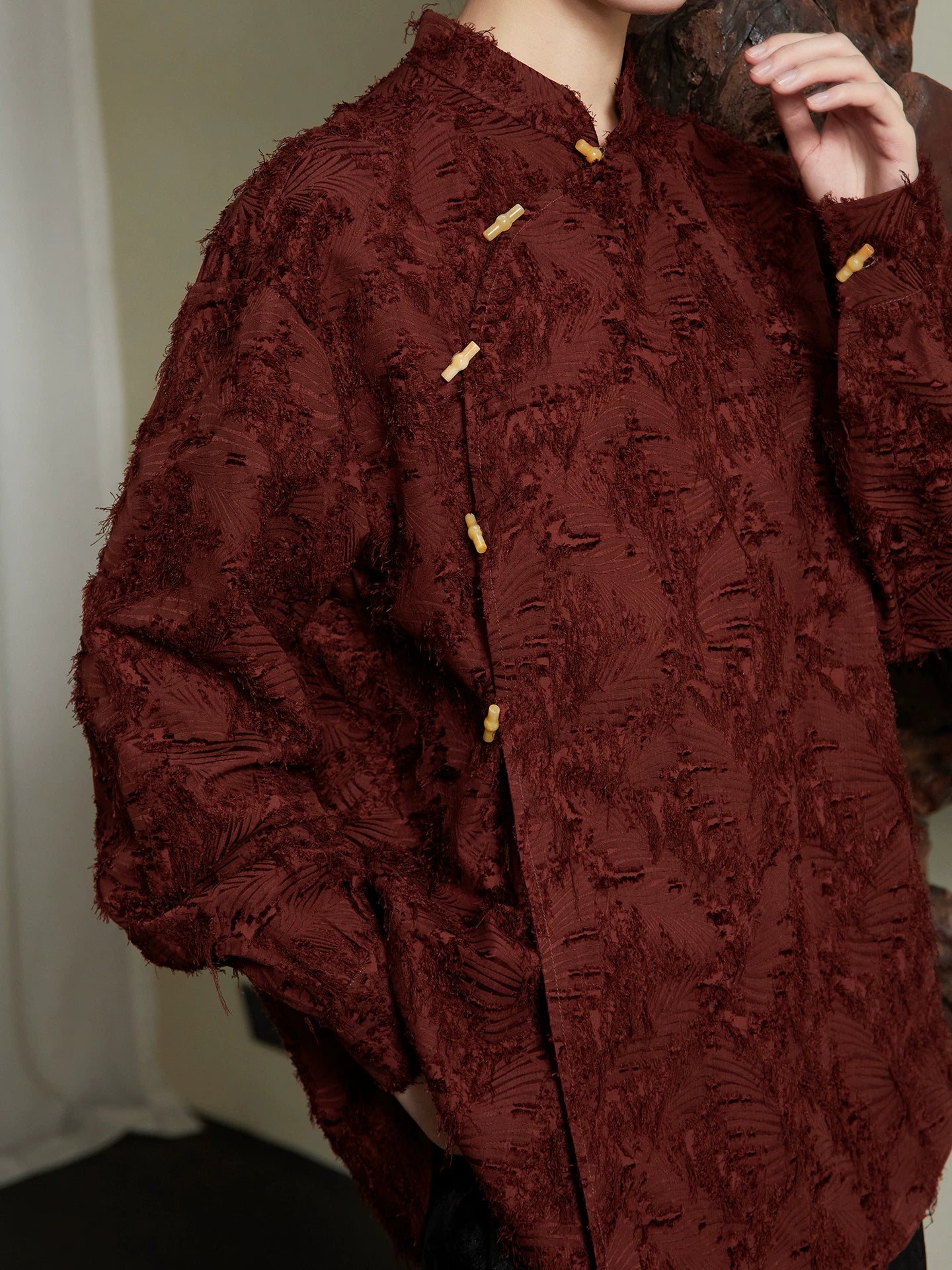 Close-up of the textured woven fabric, Mandarin collar and handcrafted frog-button details on the burgundy cotton blend blouse by Gambiered Silk.
