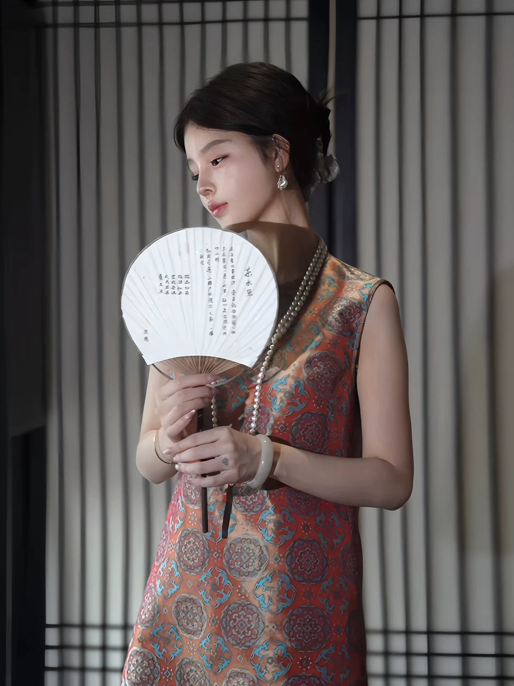 Model holding a traditional fan while wearing a vermilion Shu brocade silk dress with turquoise medallions.