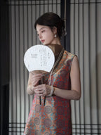 Model holding a traditional fan while wearing a vermilion Shu brocade silk dress with turquoise medallions.