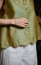 Close-up of the green loop buttons, gold piping and scalloped hem on the silk vest