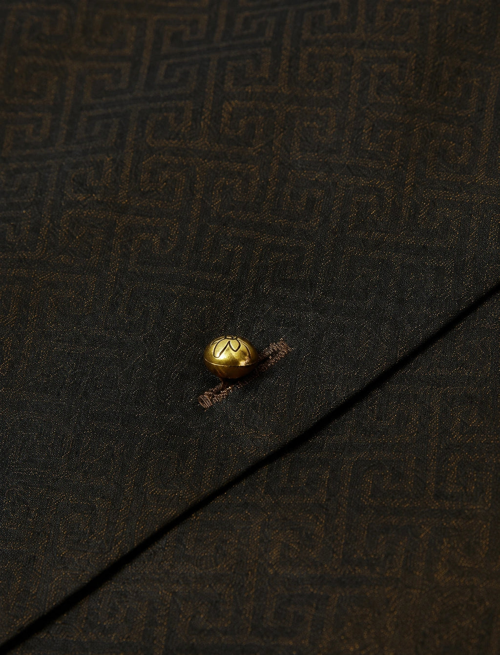 Close-up of the gold-tone button and subtle geometric jacquard texture on the dark silk-blend vest.