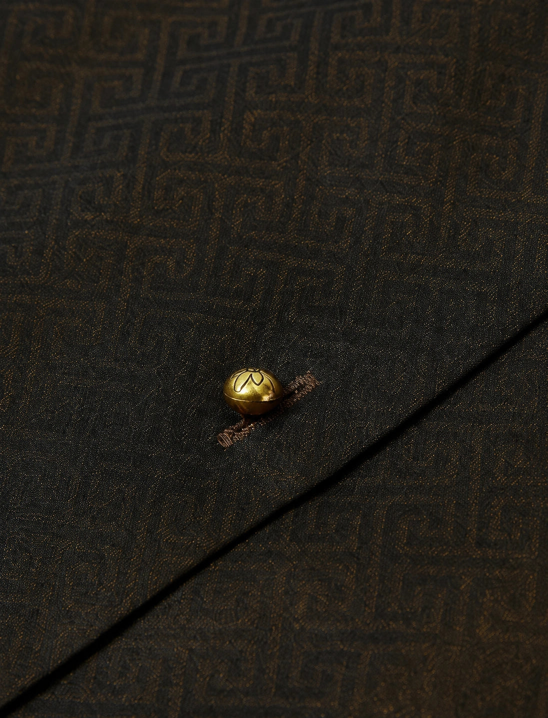 Close-up of the gold-tone button and subtle geometric jacquard texture on the dark silk-blend vest.