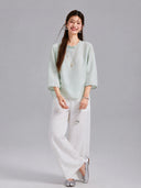 Model wearing a water blue Gambiered Silk jacquard blouse with white wide-leg trousers