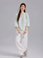 Model wearing a water blue Gambiered Silk jacquard blouse with white wide-leg trousers