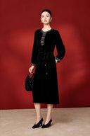Model wearing the black velvet dress with embroidered trim and a small black handbag