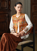 Model seated in the Gilded Ochre embroidered vest over a white blouse