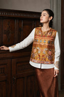Model wearing the Gilded Ochre embroidered vest beside a wooden cabinet