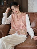 Model seated on a sofa wearing the peach vest with a white blouse
