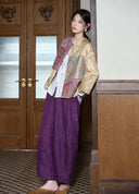 Model wearing the patchwork jacket with purple wide-leg trousers beside a wooden doorway.