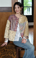 Seated model wearing the patchwork jacquard jacket over a white shirt and jeans.