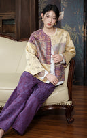 Side-angled view of a seated model wearing the colour-blocked jacket and purple trousers.