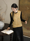 Seated model wearing a gold Chinese-style silk vest with embroidered butterfly motifs and a black skirt.