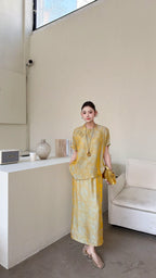 Front view of a gold New Chinese style co-ord set, featuring a short sleeve mandarin collar top with side button detail and a matching maxi skirt with side slit.